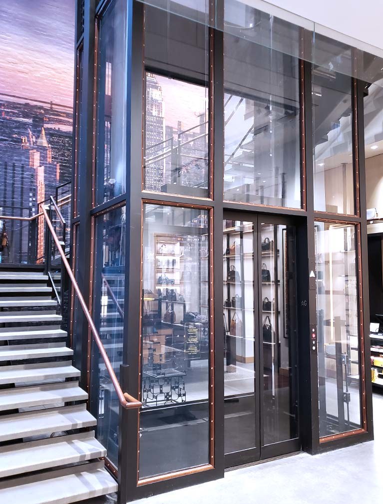 Coach First floor elevator landing reflects the brand elements with glass, wood and brass accents