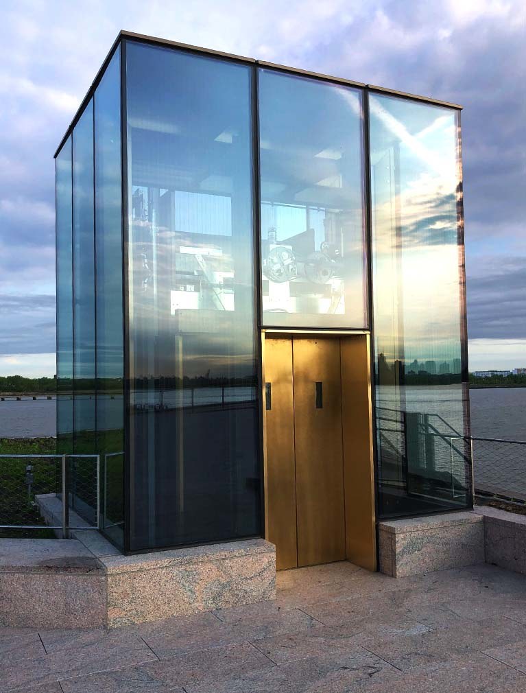 Liberty Island Museum Glass Elevator with copper doors, glass facade and sunrise reflecting in the glass