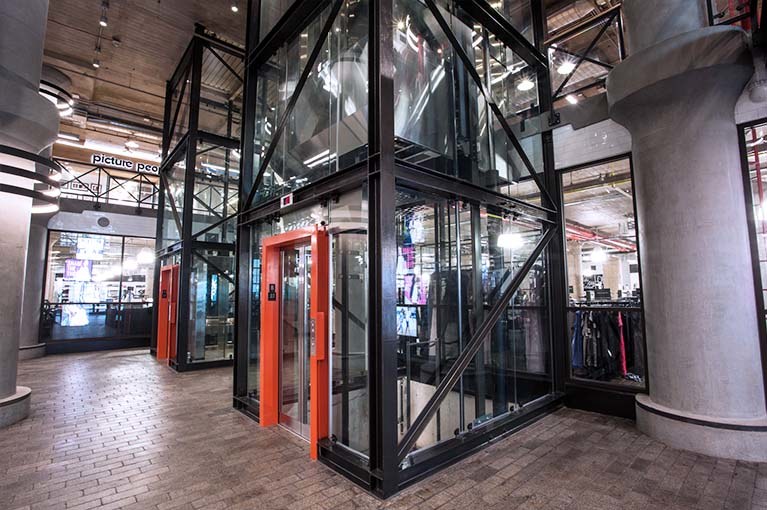 850 Third Ave, Brooklyn, double elevator bay, angle lobby, glass elevators with black steel girders & orange accent door frames