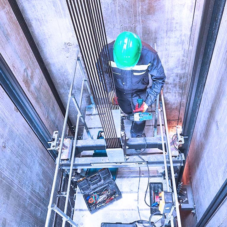 Elevator installation mechanic working on top of lift in elevator shaft